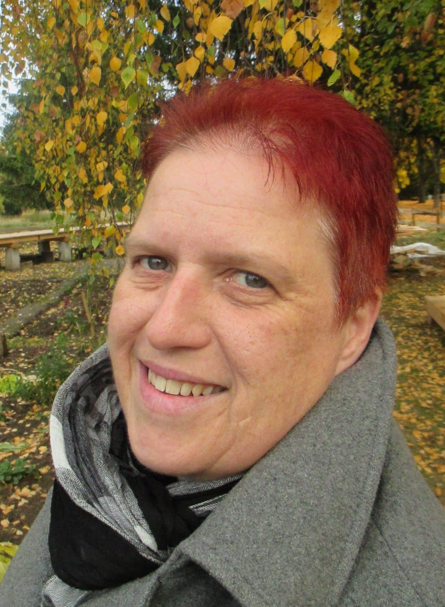 Eine Frau mit kurzen roten Haaren lächelt in die Kamera